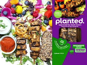 Colorful plant-based platter with grilled skewers and sauces beside purple 'planted' meat packaging.
