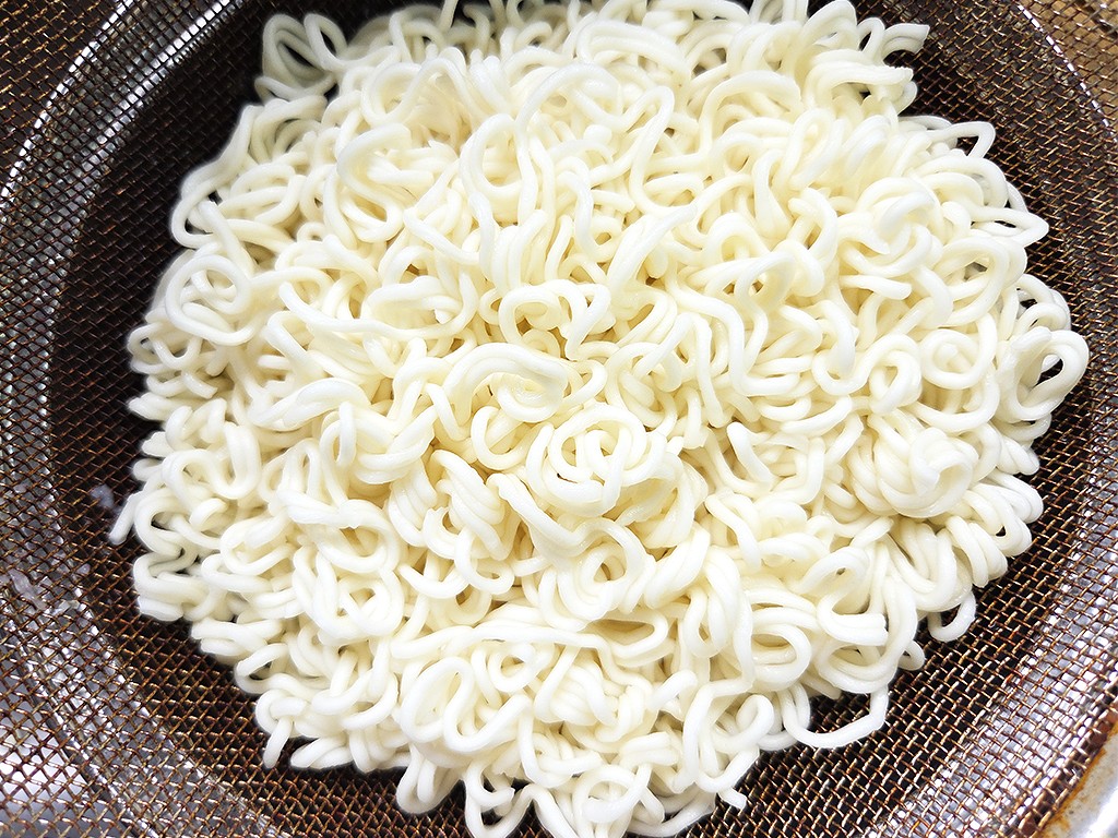 Pile of pale white, curly ramen noodles resting in a brown metal mesh strainer.