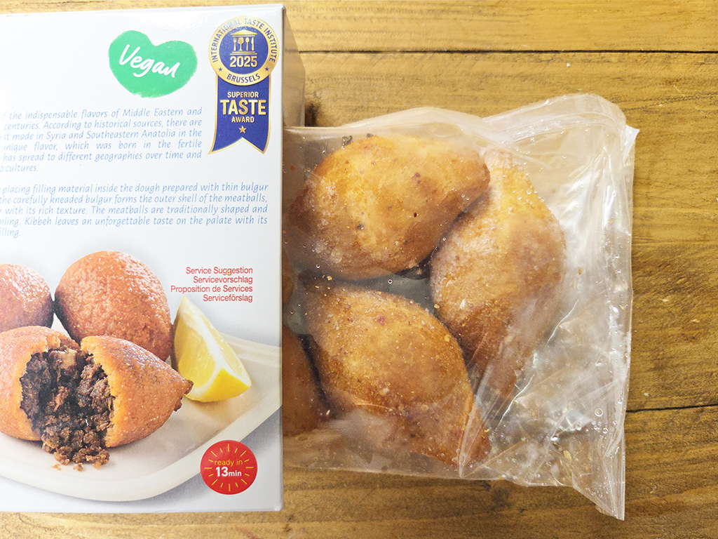 Vegan boxed snacks beside a bag of fried vegan meatballs on a wooden surface.