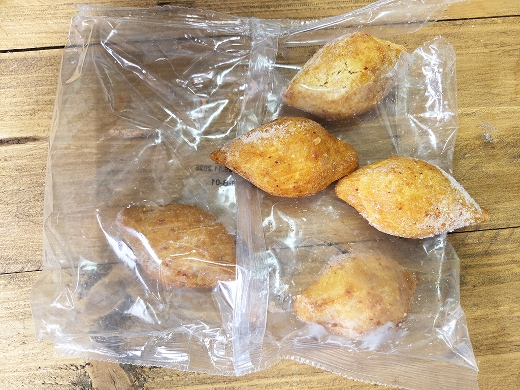 Five small golden pastries inside a clear plastic bag on a wooden table.