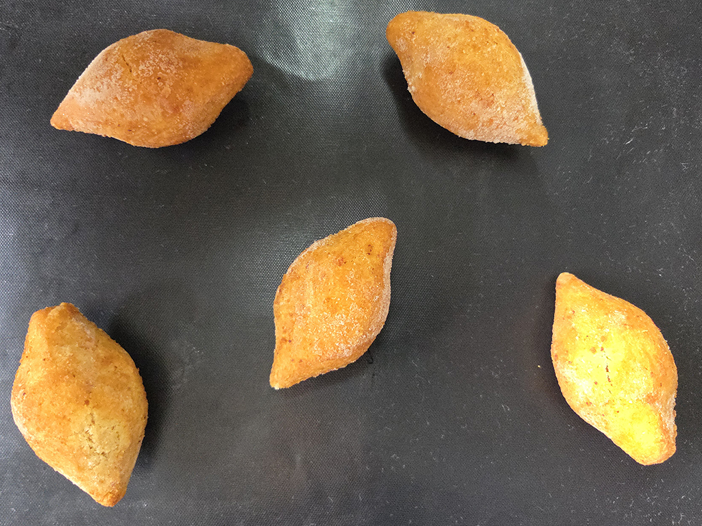 Five orange baked pastries arranged on a dark baking sheet on a black surface.