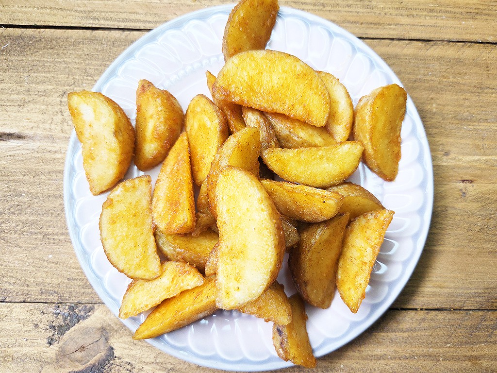 Golden potato wedges piled on a white plate, resting on a wooden table.
