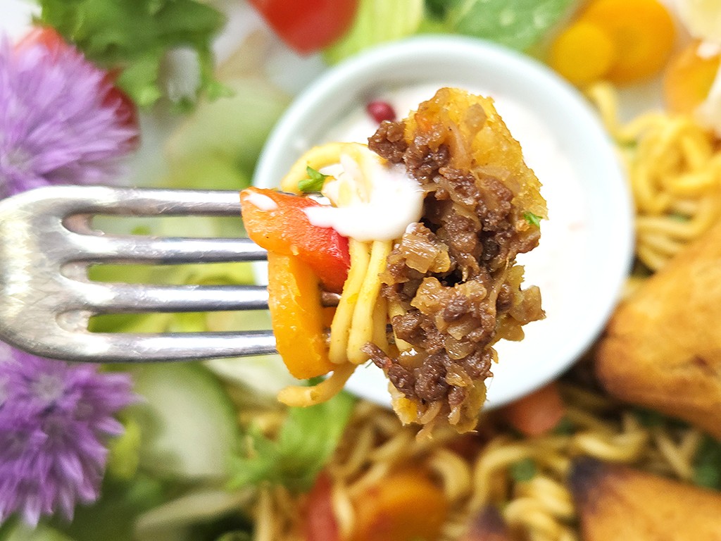 Forkful of spaghetti with ground beef, peppers, and a dollop of sauce, held over a plate of pasta in the background.