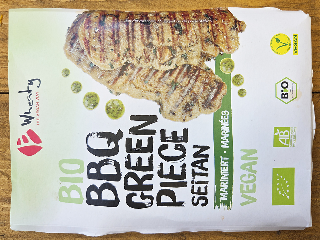 Wheaty | Bio BBQ Green Piece Seitan | Herzschatz Front of vegan organic veggie burger packaging with grilled burger slices on top, green BIO label and VEGAN seal visible.