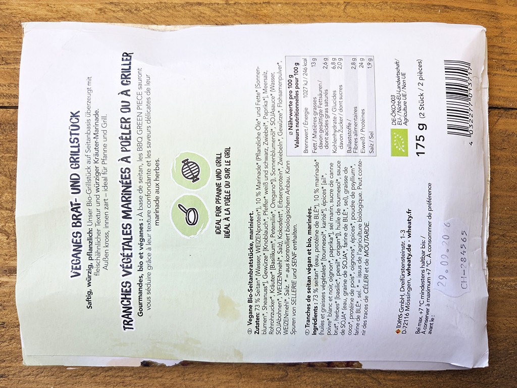 Wheaty | Bio BBQ Green Piece Seitan | Herzschatz Back side of a white vegan product package with German text, nutrition table, barcode, and 175 g weight on a wooden surface.