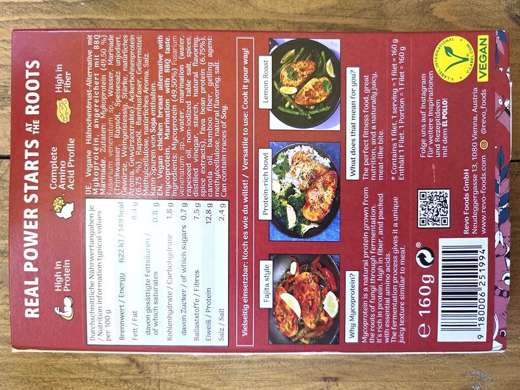 Revo | El Pollo | Herzschatz Red rectangular vegan product box showing nutrition facts and pictures of plated meals, barcode, and vegan logo on a wooden surface back panel.