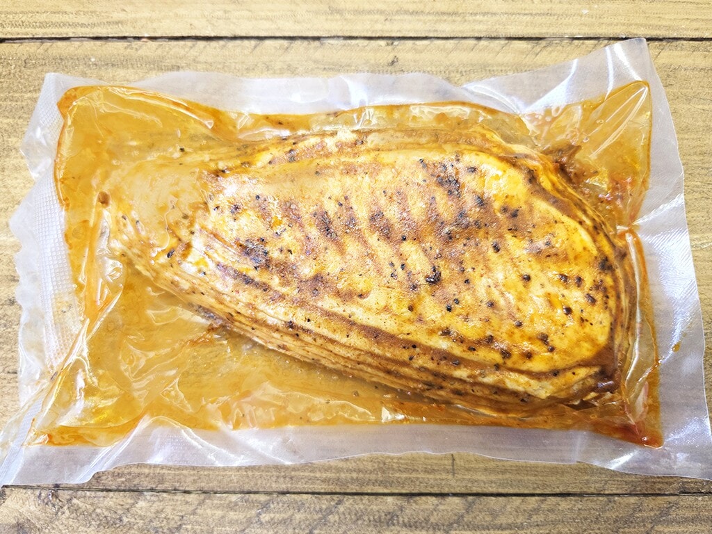 Revo | El Pollo | Herzschatz Vacuum-sealed raw turkey breast in marinade resting on a wooden surface.