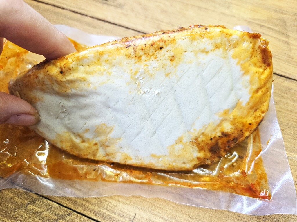Revo | El Pollo | Herzschatz Wedge of soft white cheese on plastic with orange sauce, held by a hand on a wooden table.