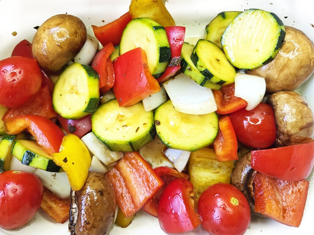 Revo | El Pollo | Herzschatz Assorted roasted vegetables: zucchini, bell peppers, onions, cherry tomatoes, and mushrooms in a white tray.