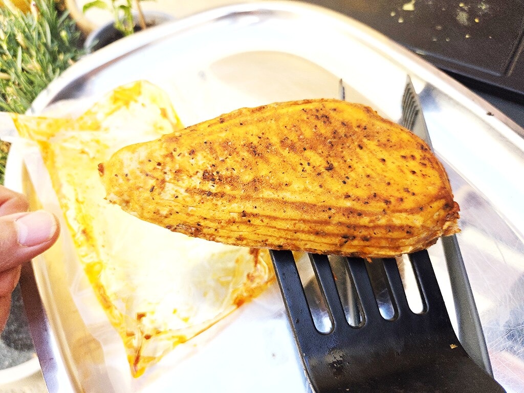 Revo | El Pollo | Herzschatz Golden-brown fried chicken piece held on a slotted spatula over a metal tray/plate.