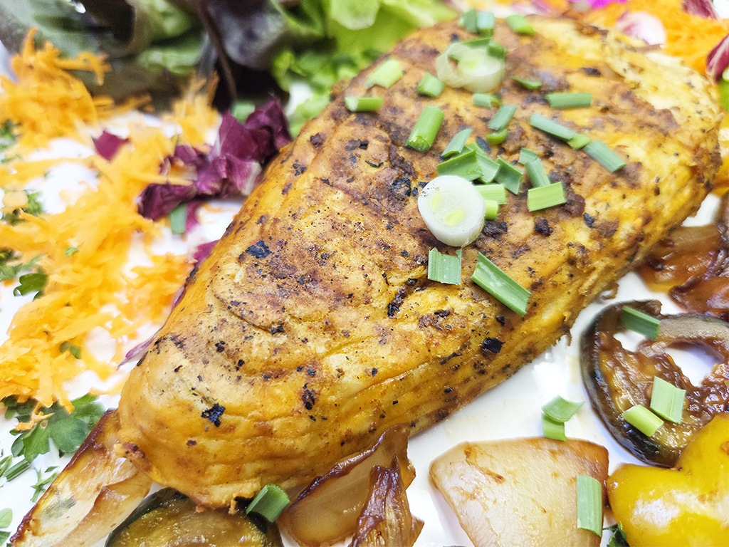 Revo | El Pollo | Herzschatz Herb-roasted chicken breast with green onion garnish on a bed of roasted vegetables on a white plate