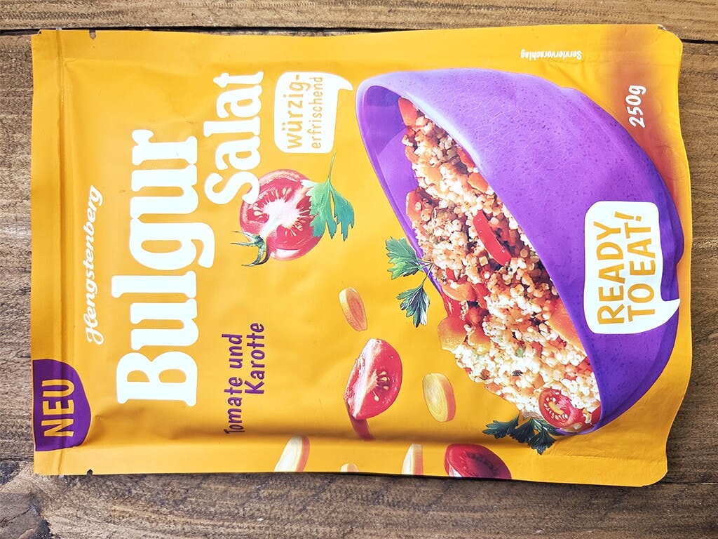 Hengstenberg | Bulgur Salat mit Tomate und Karotte | Herzschatz Bright yellow ready-to-eat meal pouch with a purple bowl of grain, featuring the label 'READY TO EAT' and text 'Tomate und Kartoffel'.