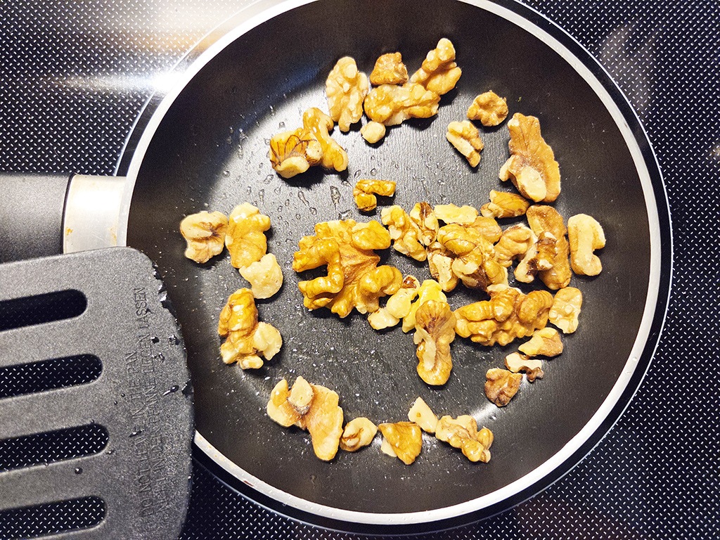 Hengstenberg | Bulgur Salat mit Tomate und Karotte | Herzschatz Walnut pieces toasting in a nonstick skillet with a spatula resting at the edge.
