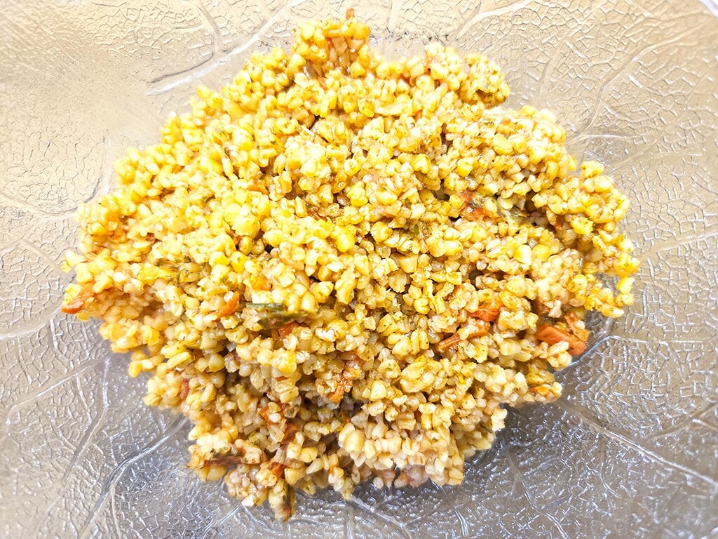 Hengstenberg | Bulgur Salat mit Tomate und Karotte | Herzschatz Mound of fried rice with corn and small vegetable pieces on a textured glass plate, bright and yellowish.