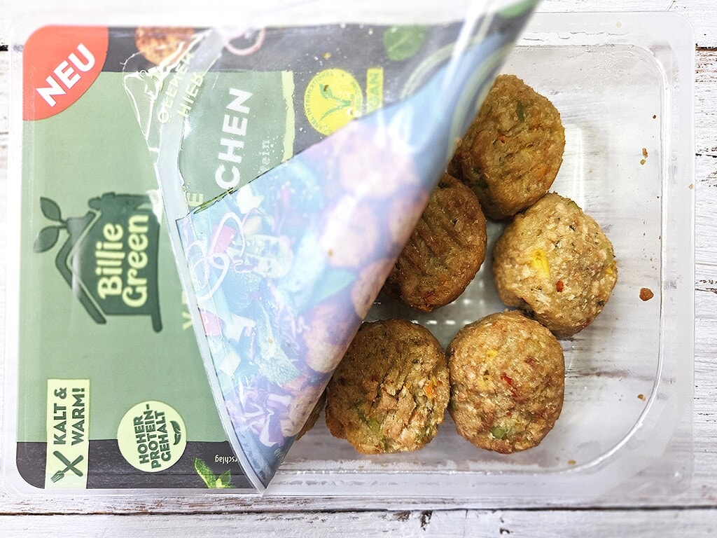 Six baked veggie meatballs in a clear plastic container, partially opened to reveal the green-packaged product with a red 'NEU' label.