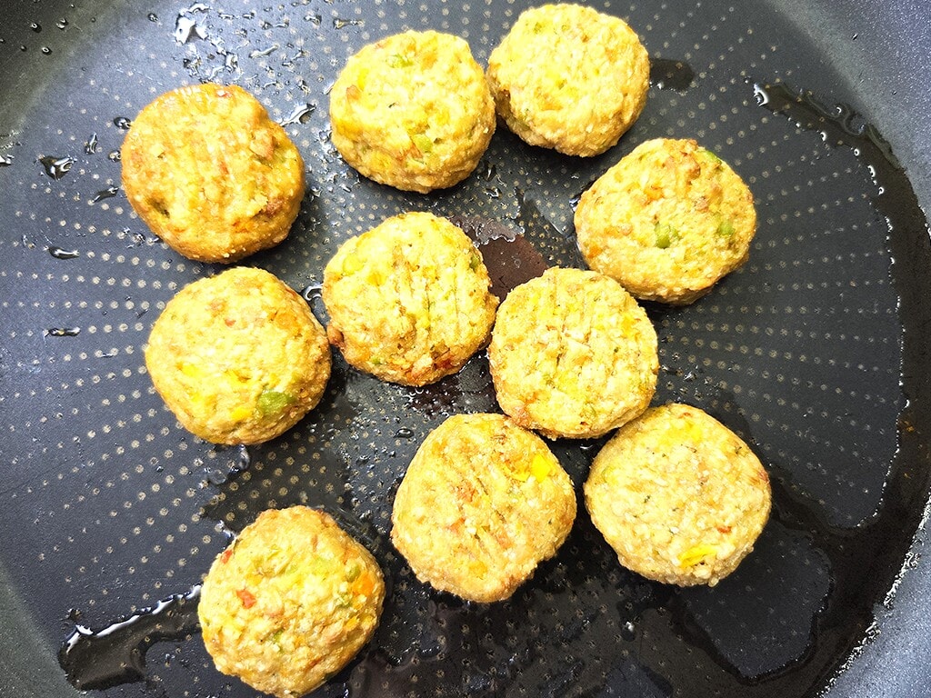 Golden fried falafel balls cooking in a black nonstick skillet with a bit of oil.