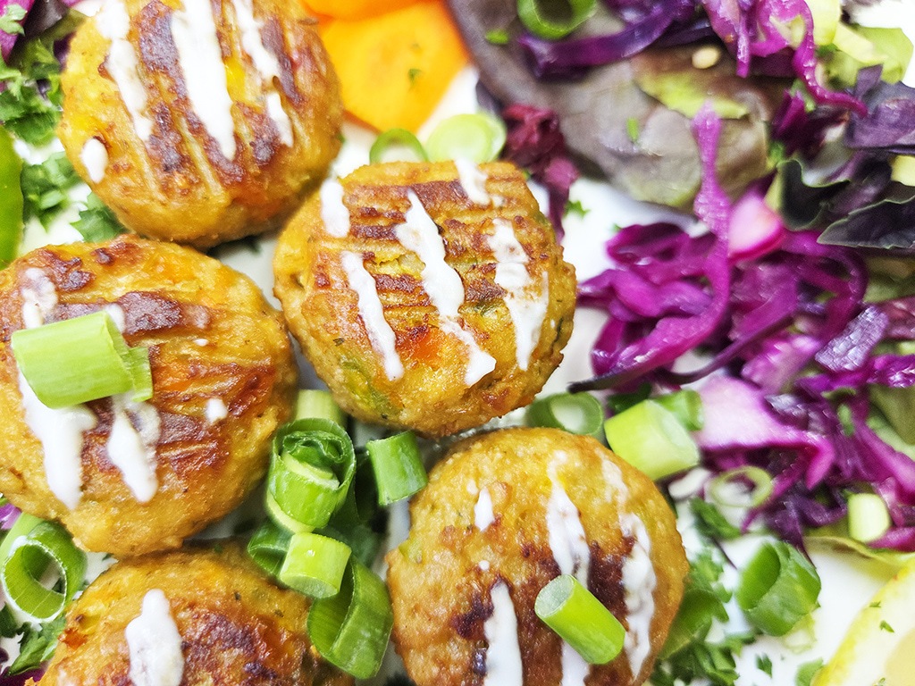 Crispy croquettes topped with white drizzle and green onions, served with a colorful salad including purple cabbage slaw.