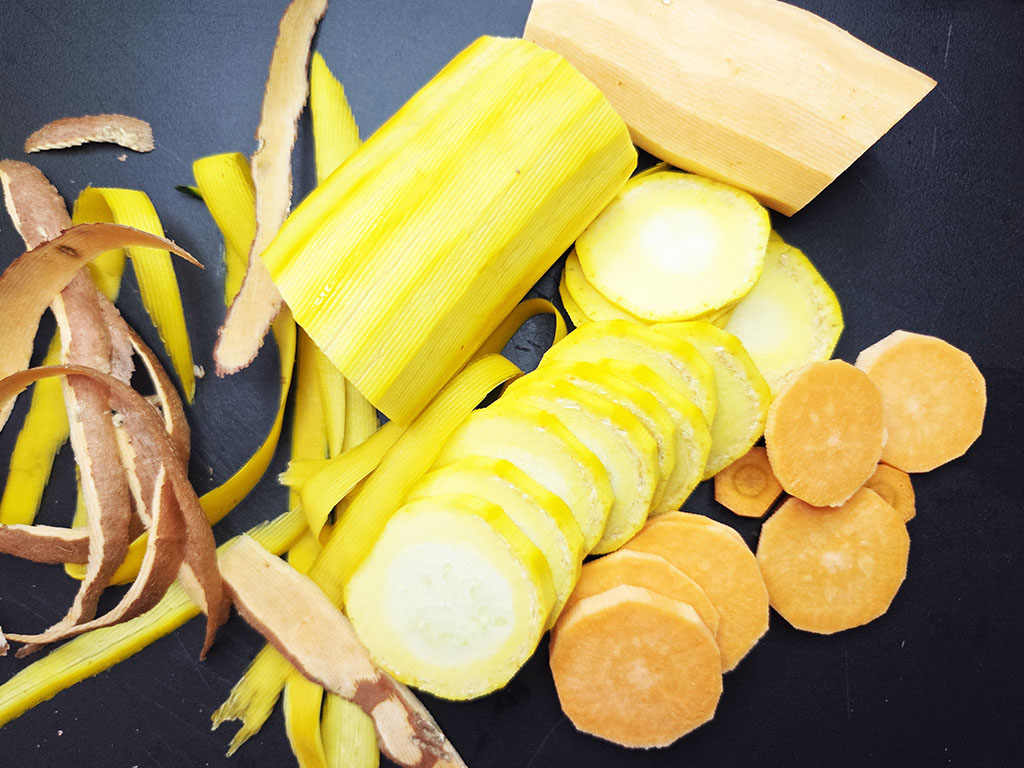 Tofoo & Co | Smoked Tofu | Herzschatz Assorted yellow vegetables sliced on a dark surface, including round plantain chips and orange carrot coins.
