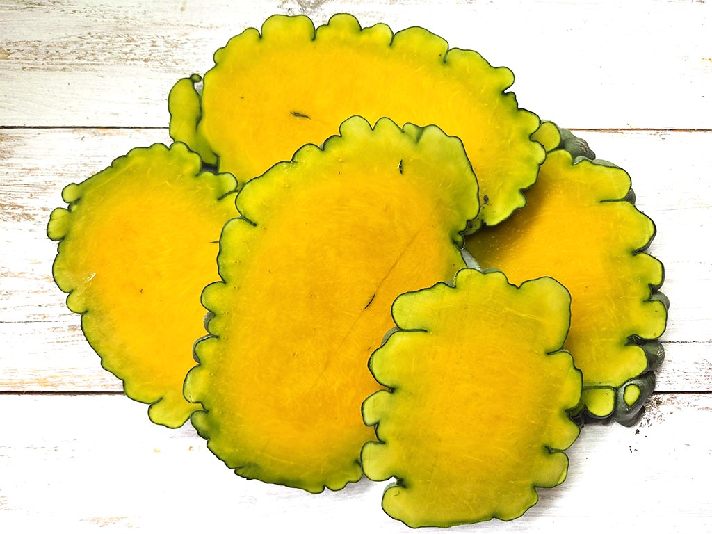 Cluster of yellow scalloped-edged fruit slices with green rims arranged on a white wooden surface, close-up.