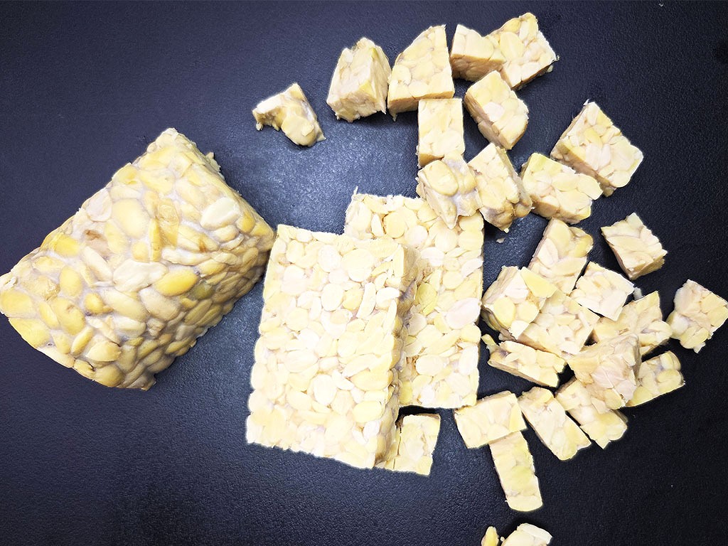 Broken pieces of almond brittle spread on a dark surface with a small almond-populated block on the left side.