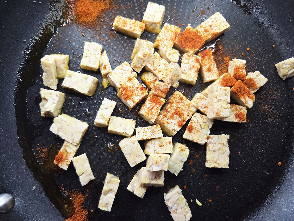 Diced firm tofu browning in a dark skillet with paprika sprinkled on top