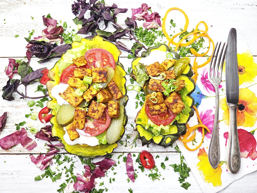 Two vibrant veggie tacos topped with crispy tofu, tomato, pickles and greens on a white wooden table, colorful and fresh.