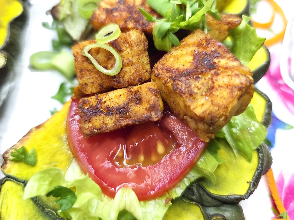 Close-up of crispy fried tofu cubes stacked on a tomato slice in a lettuce and veggie wrap, topped with green onions and greens.