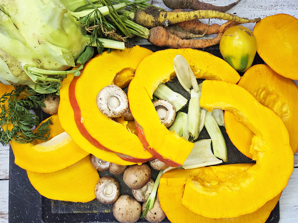 Planted. | Filet-Würfel a la mexicana | Herzschatz Sliced orange pumpkin with mushrooms, leeks, carrots and fresh herbs on a dark cutting board