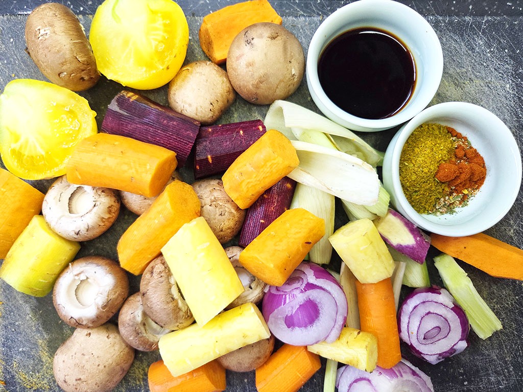 Planted. | Filet-Würfel a la mexicana | Herzschatz Colorful assortment of chopped vegetables (carrots, potatoes, onions, mushrooms, celery) with spice bowls on a dark surface, ready for cooking.