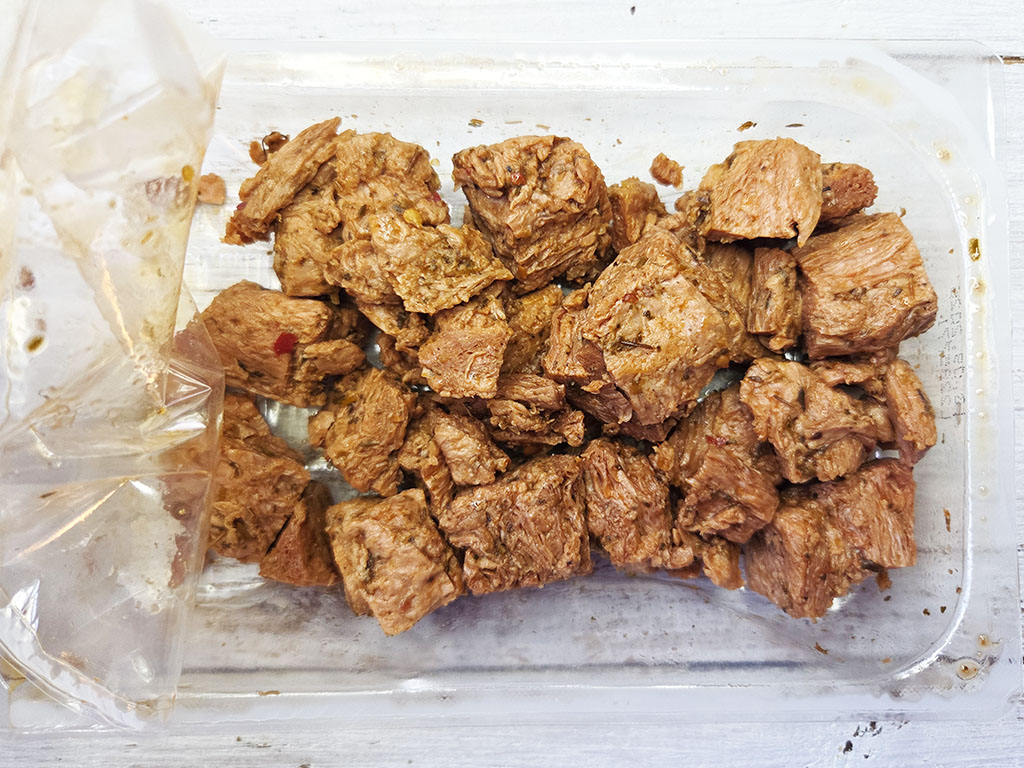 Planted. | Filet-Würfel a la mexicana | Herzschatz Chunks of cooked beef in a clear plastic tray, with a plastic bag on the left edge.