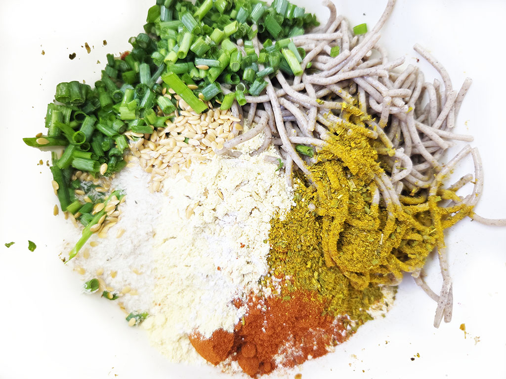 Planted. | Filet-Würfel a la mexicana | Herzschatz Pile of ingredients for seasoned noodles: soba noodles, chopped green onions, sesame seeds, flour, curry powder, paprika, and chili powder intermingled on a white plate