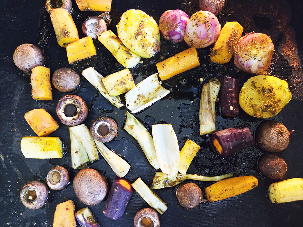 Planted. | Filet-Würfel a la mexicana | Herzschatz Assorted roasted root vegetables on a dark grill pan, including yellow squash, red onions, beets, and parsnips cut into chunks and rounds.