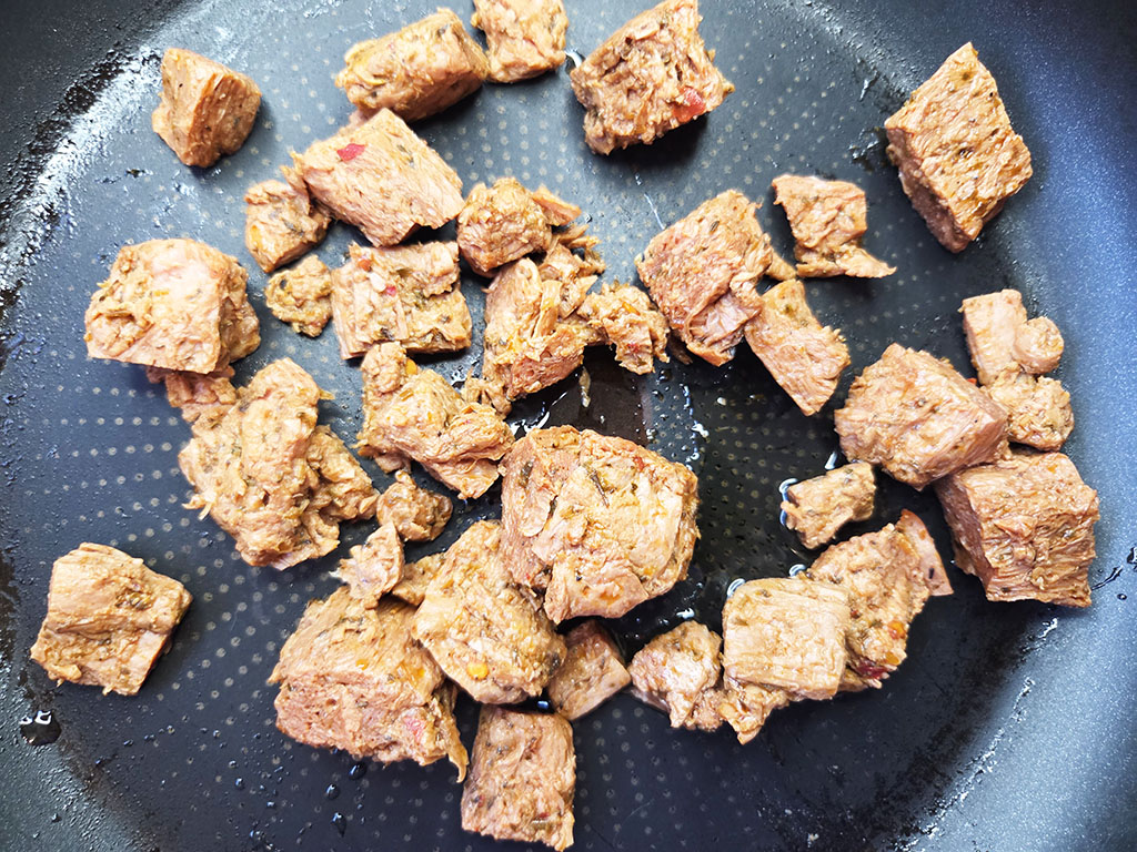 Planted. | Filet-Würfel a la mexicana | Herzschatz Cubed browned meat pieces scattered in a frying pan with a dark nonstick surface.