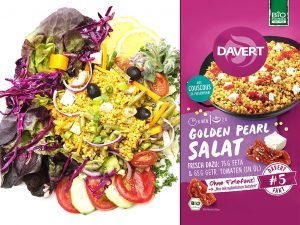 Colorful couscous salad with greens, tomatoes and olives on a plate, beside a purple Davert Golden Pearl Salat package.