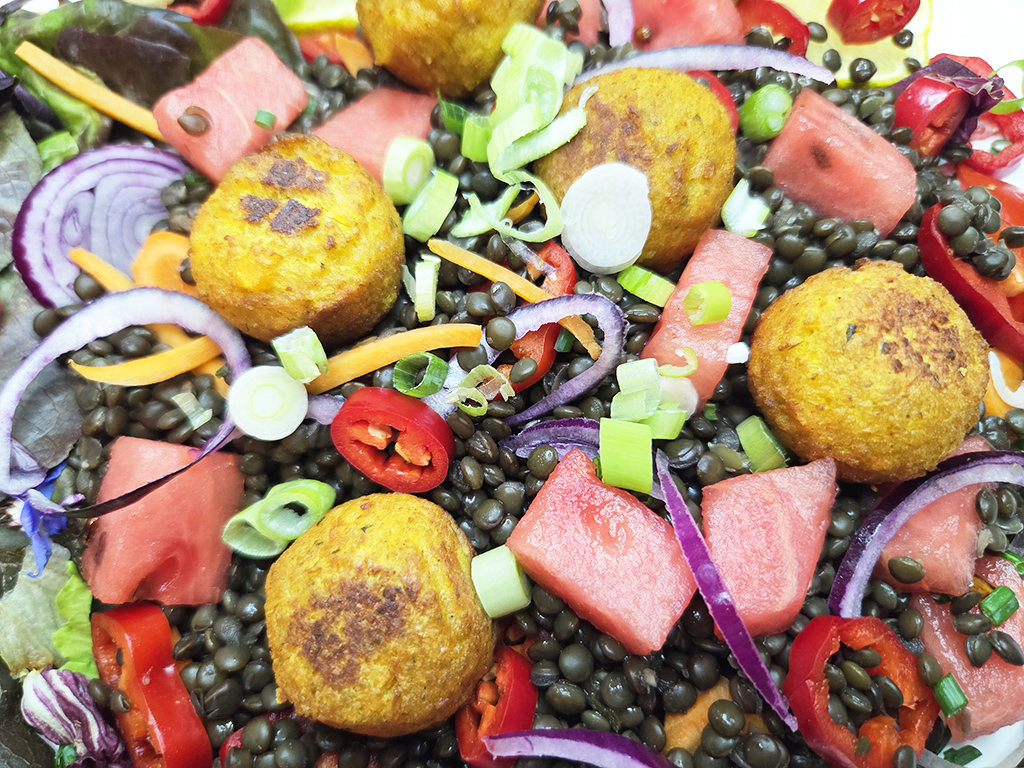 SOTO | Falafel Traditionell | Herzschatz Colorful mixed salad with golden falafel balls, black beluga lentils, watermelon cubes, red onion slices, carrot ribbons, cucumber, peppers, and scallions.