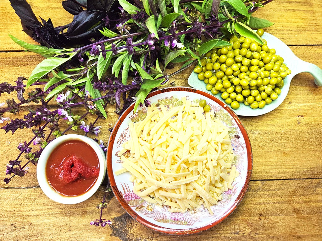 Pile of grated cheese on a decorative plate with fresh herbs and a side of tomato sauce, peas, on a wooden table.