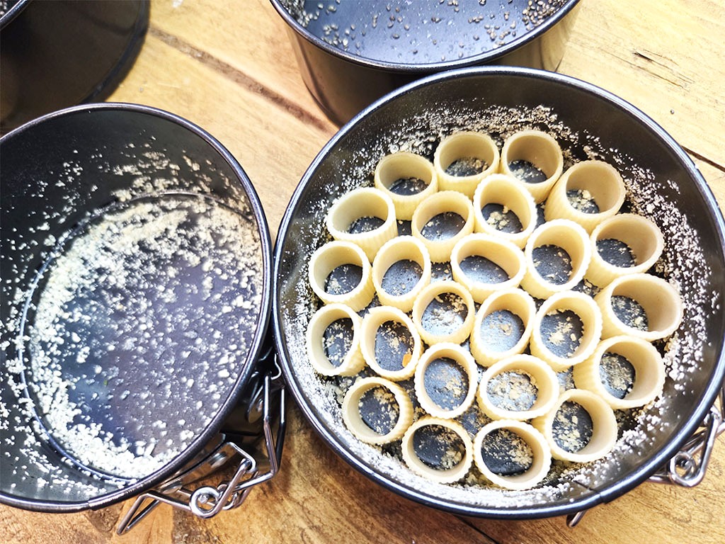 Round baking pan filled with many ring-shaped pasta pieces (tubetti/ring macaroni) arranged in neat circles on a lightly floured surface.