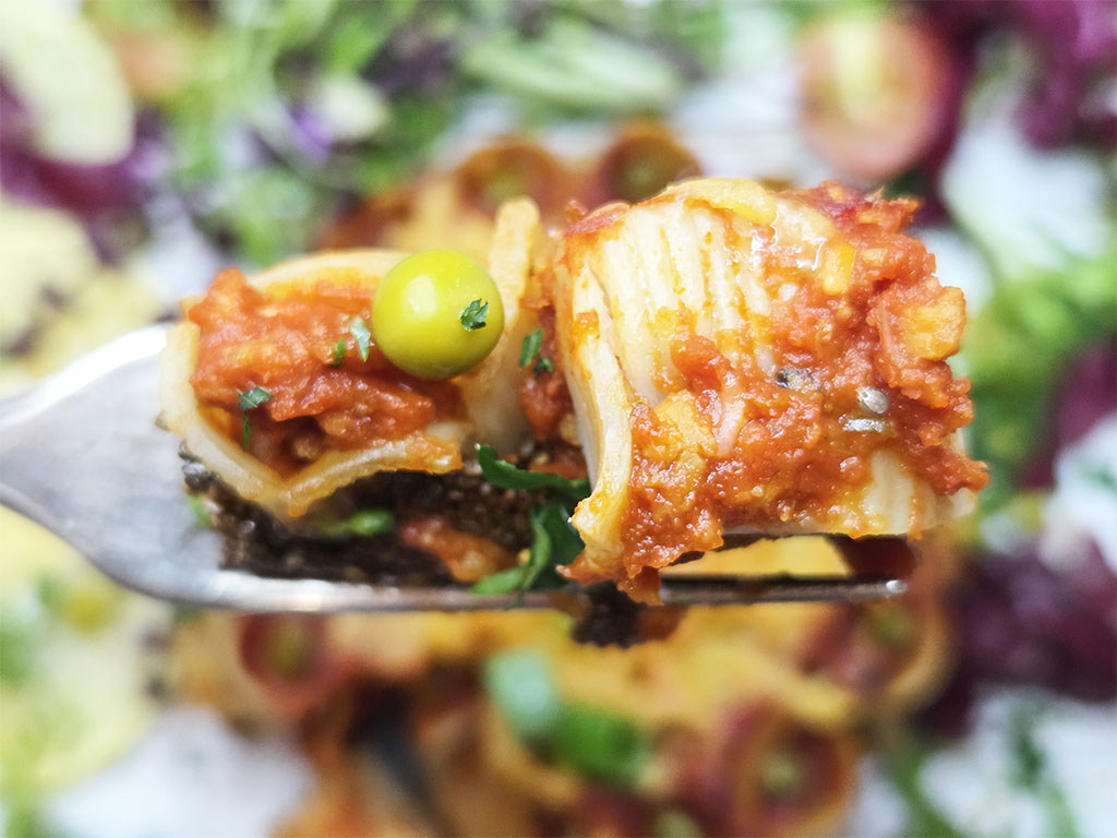 Close-up of spaghetti on a fork with chunky tomato sauce, a green olive, and herbs.